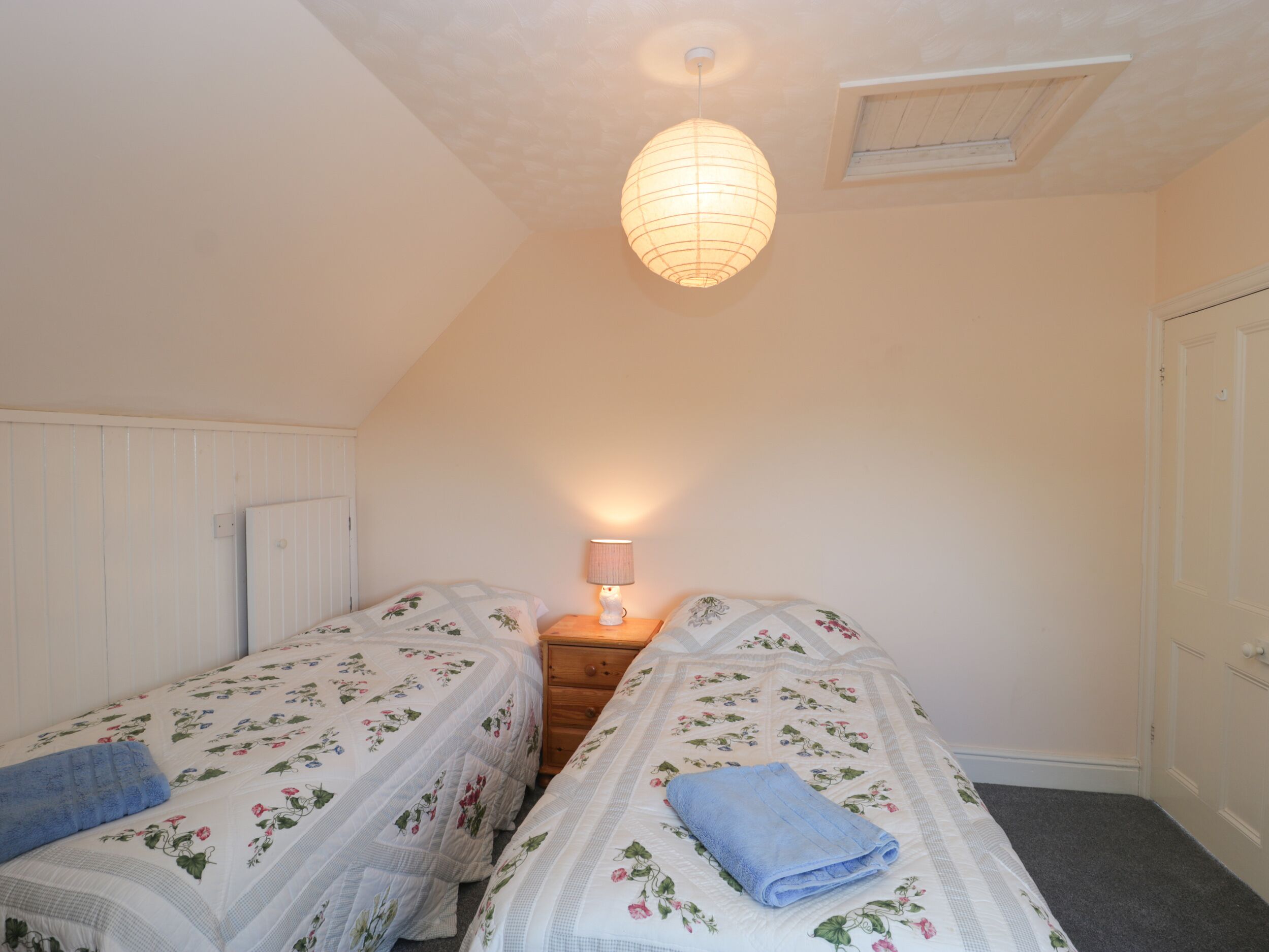 A bedroom with two single beds, a nightstand with a lamp, a wooden dresser, and a ceiling light fixture.