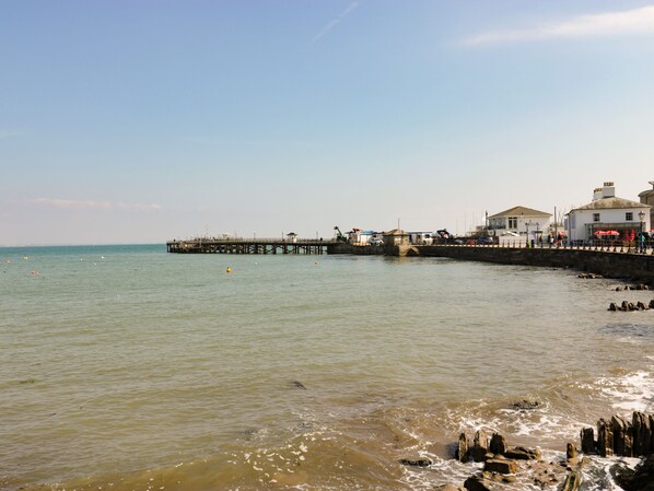 Eine Pier, die sich über ruhiges Wasser erstreckt, mit einem kleinen Gebäude und einer weißen Struktur auf der rechten Seite.