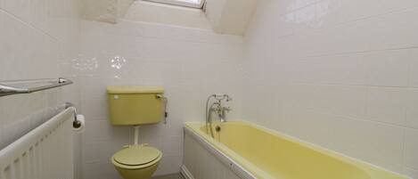 A small, narrow bathroom with white tiles, a yellow toilet, a yellow bathtub, and a skylight above the toilet.