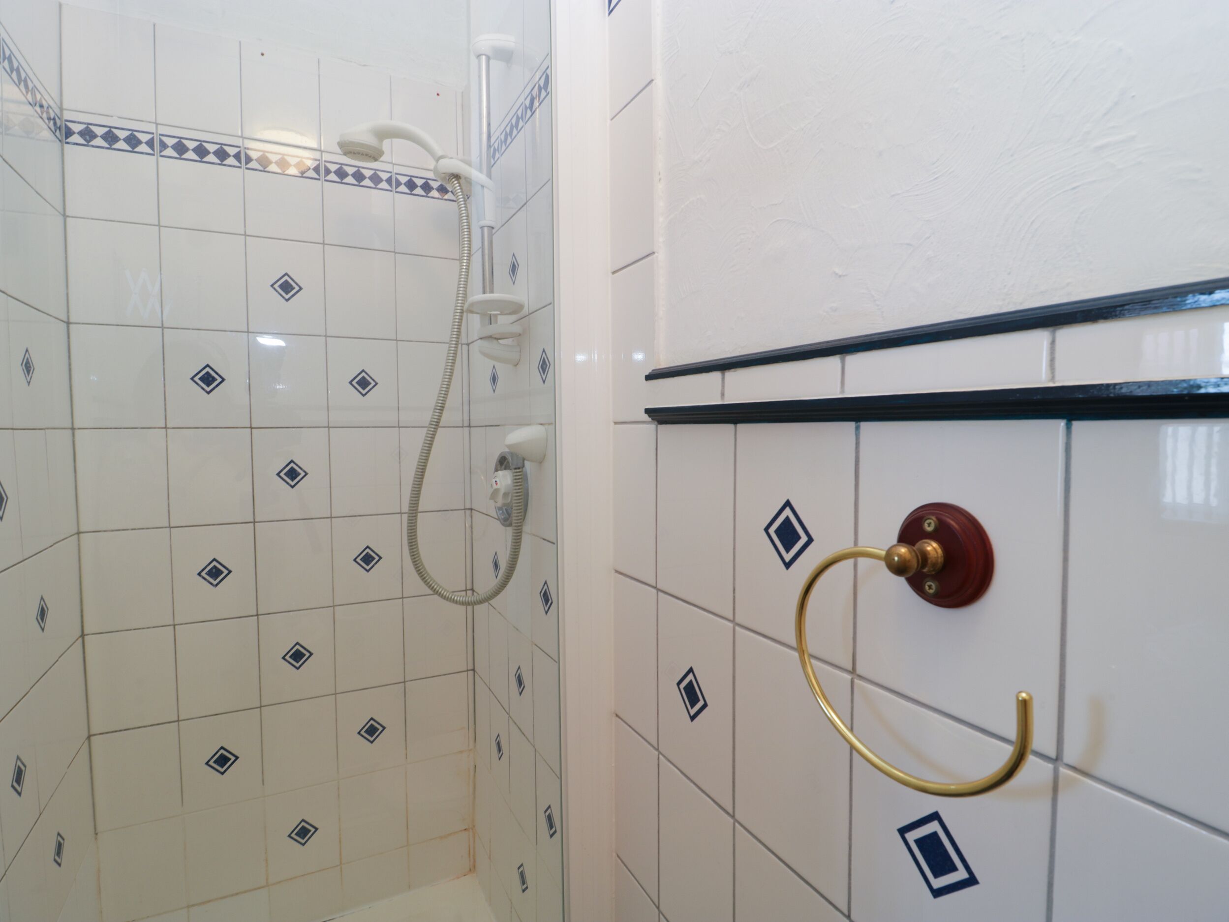 Une salle de bain avec des murs recouverts de carreaux blancs, un espace douche et un porte-serviettes avec un support à serviettes de couleur dorée.