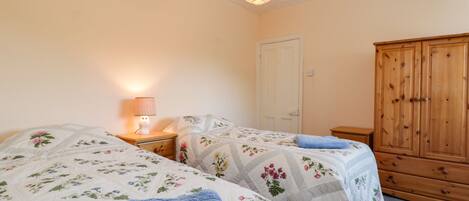 A bedroom with two beds, a wooden wardrobe, and a nightstand with a lamp.