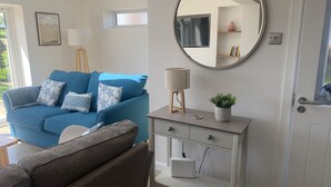 A living room with a blue sofa, a round mirror, a small table with a lamp, and a potted plant.