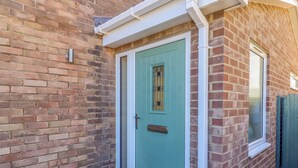 A brick house with a teal door, a window, and a small potted plant.