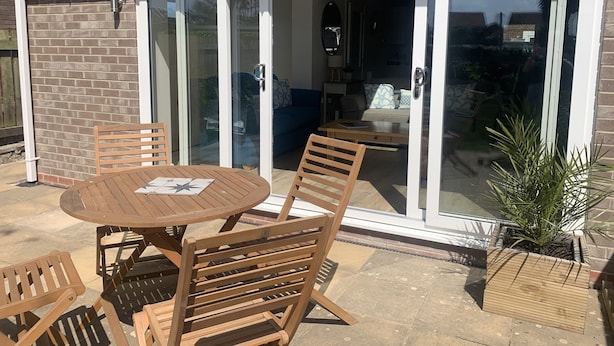 A patio with a round wooden table and chairs, a sliding glass door leading to an interior space with a sofa and a coffee table.