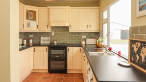 A kitchen with light-colored cabinets, a black stove, and a window providing natural light. - Newtown East (Newtown East)