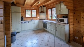 A wooden cabin kitchen with a tiled floor, a stove, a microwave, and a window overlooking a garden. - Cosy Chalet near Ski Resorts with Terrace and Forest Trails (Vagney)