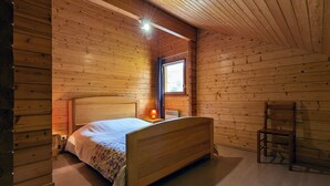 A wooden cabin bedroom with a bed, a nightstand, a lamp, and a window. - Cosy Chalet near Ski Resorts with Terrace and Forest Trails (Vagney)