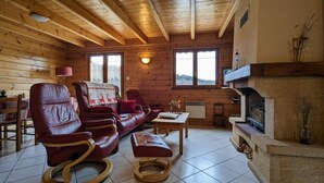 A cozy log cabin interior with a leather sofa, a rocking chair, a fireplace, and large windows. - Cosy Chalet near Ski Resorts with Terrace and Forest Trails (Vagney)