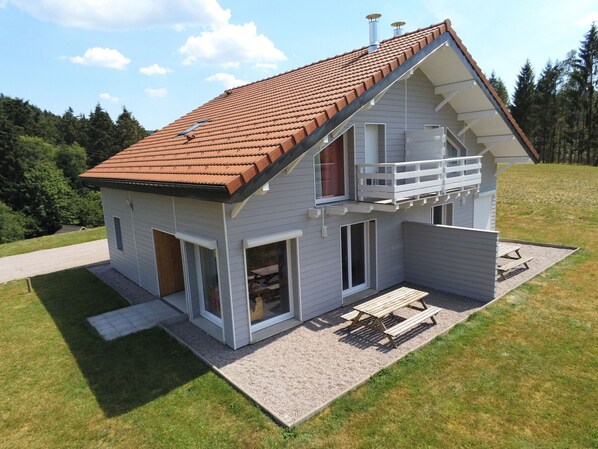 A two-story house with a red-tiled roof, a balcony, and a patio area with a table and benches.