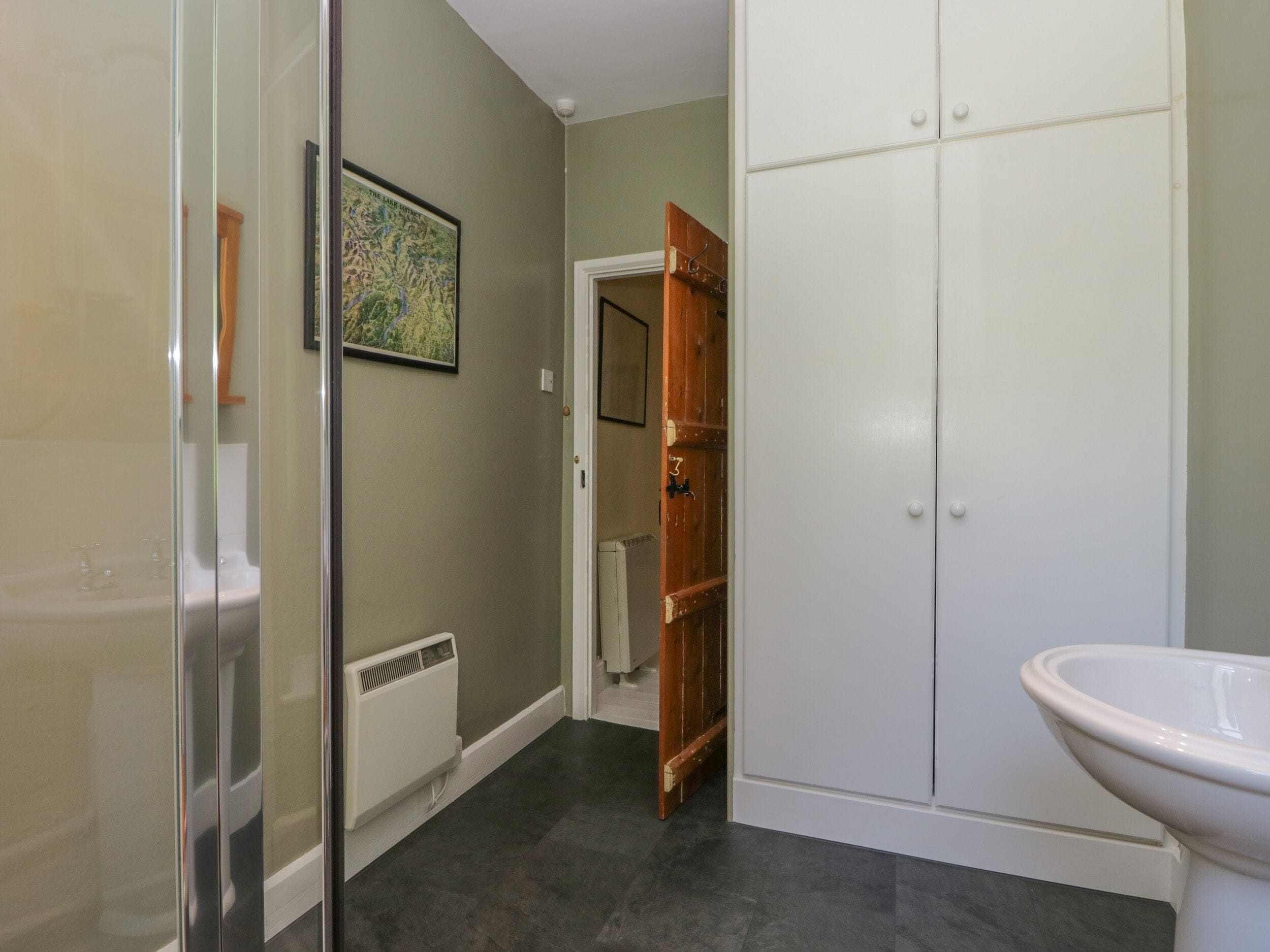 Een badkamer met een douchecabine van glas, een wit toilet en een houten deur naar een gang.