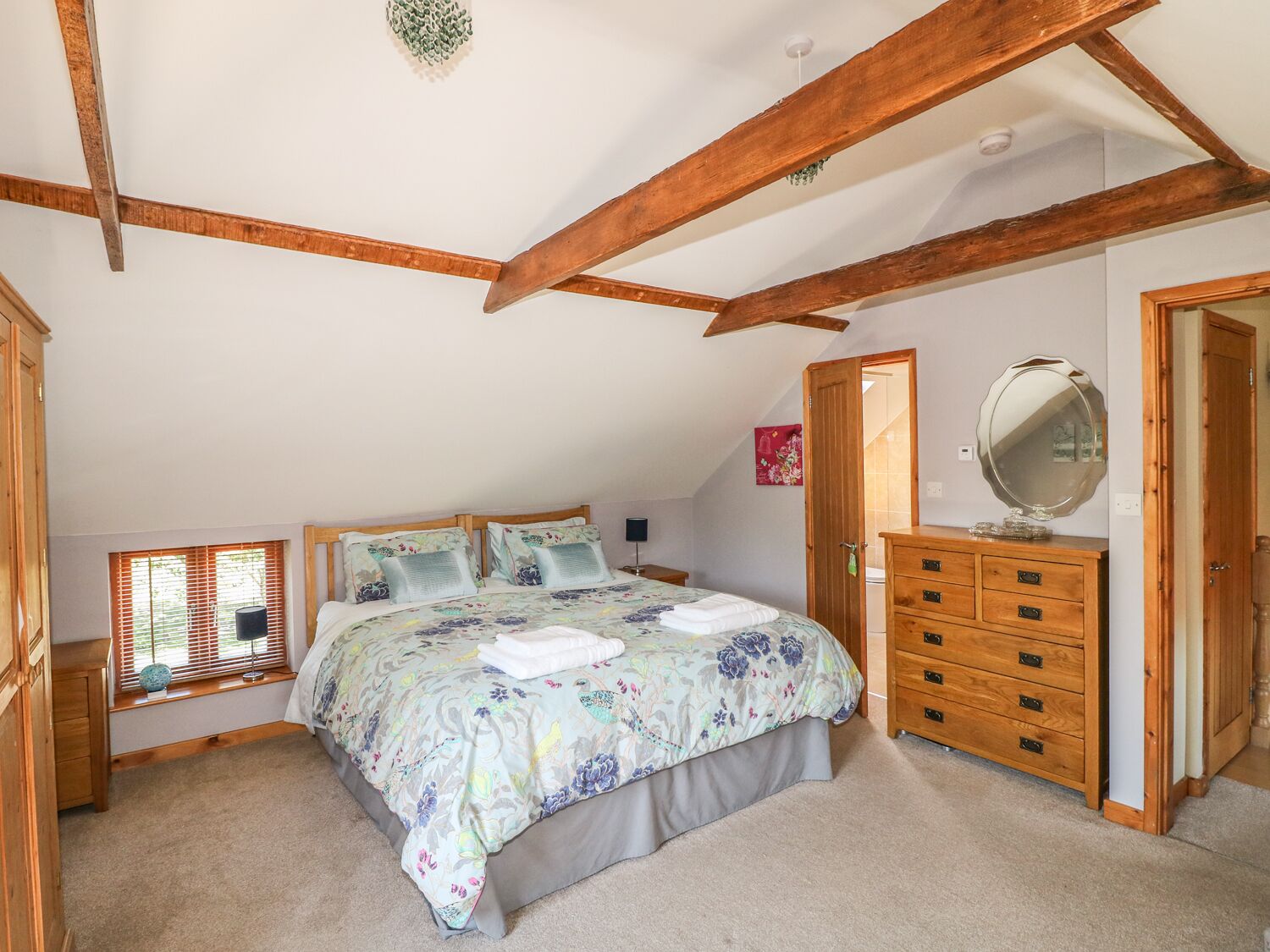 A bedroom with a bed, wooden dresser, and a window with blinds.