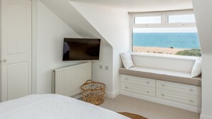 A bedroom with a view of the sea, a bed, a TV, a window seat, and a radiator. - Beach Haven (Dorchester)