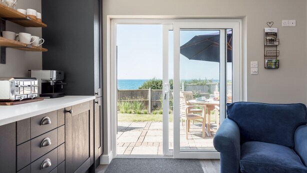A modern kitchen with a sliding glass door leading to an outdoor patio with a view of the sea. - Beach Haven (Dorchester)