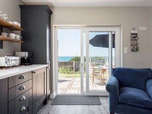 A modern kitchen with a sliding glass door leading to an outdoor patio with a view of the sea. - Beach Haven (Dorchester)