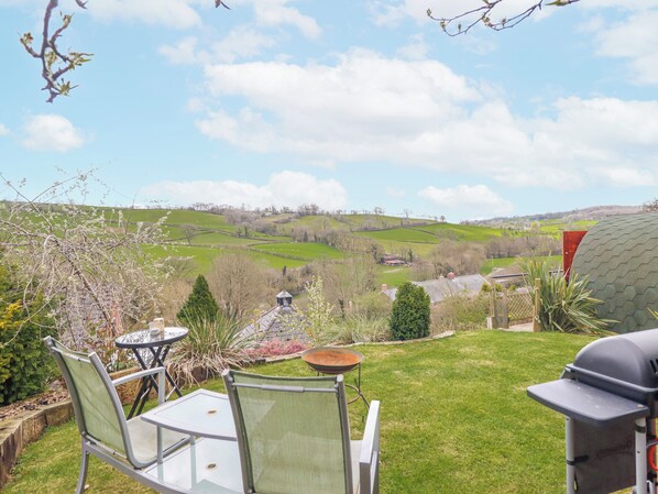 Un patio con una mesa, sillas, una parrilla y vistas a colinas onduladas.