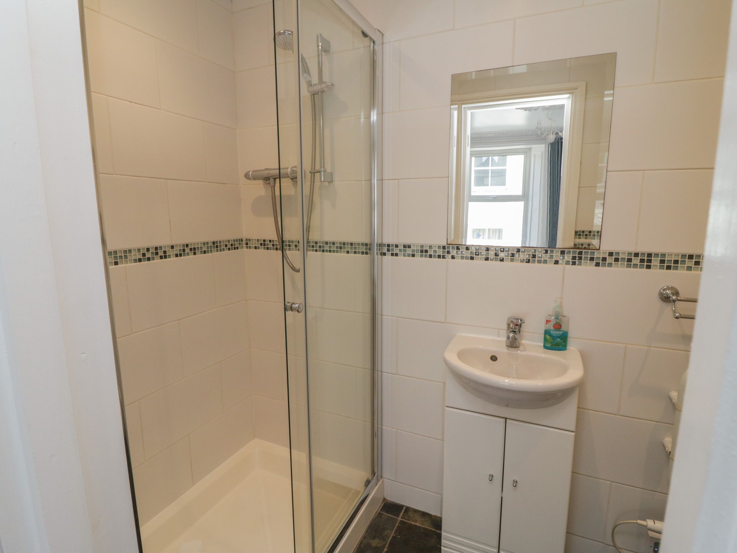 A bathroom with a glass-enclosed shower, a sink with a mirror above it, and tiled walls.