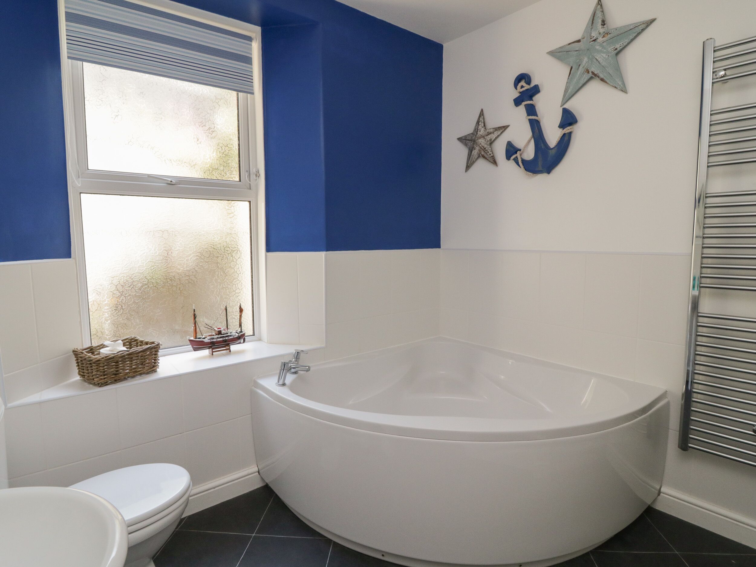 A bathroom with a white bathtub, a white toilet, and a window with a decorative ship model.