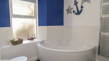 A bathroom with a white bathtub, a white toilet, and a window with a decorative ship model.