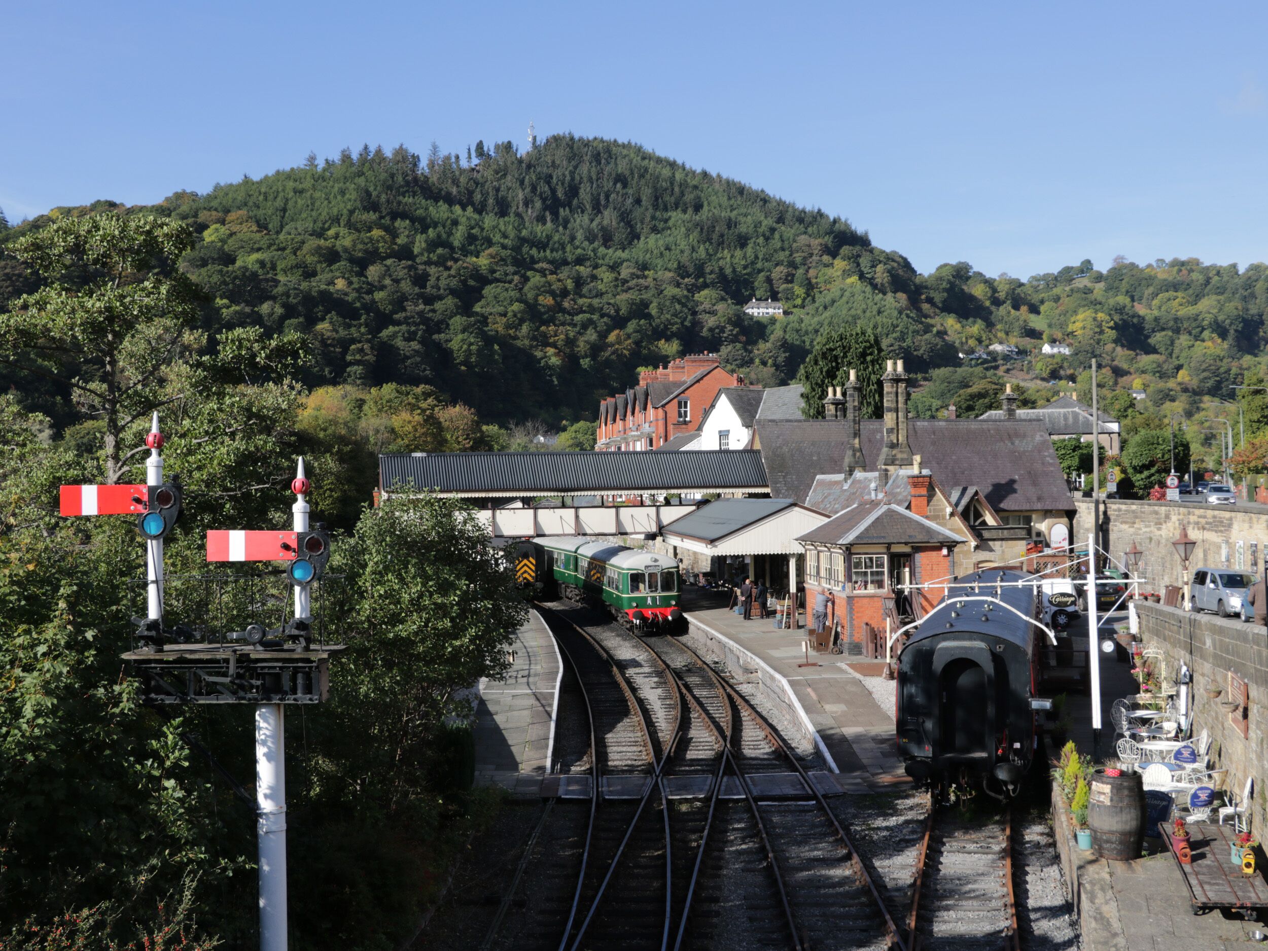 A railway station with tracks, a platform, and a building with a traditional architectural style.