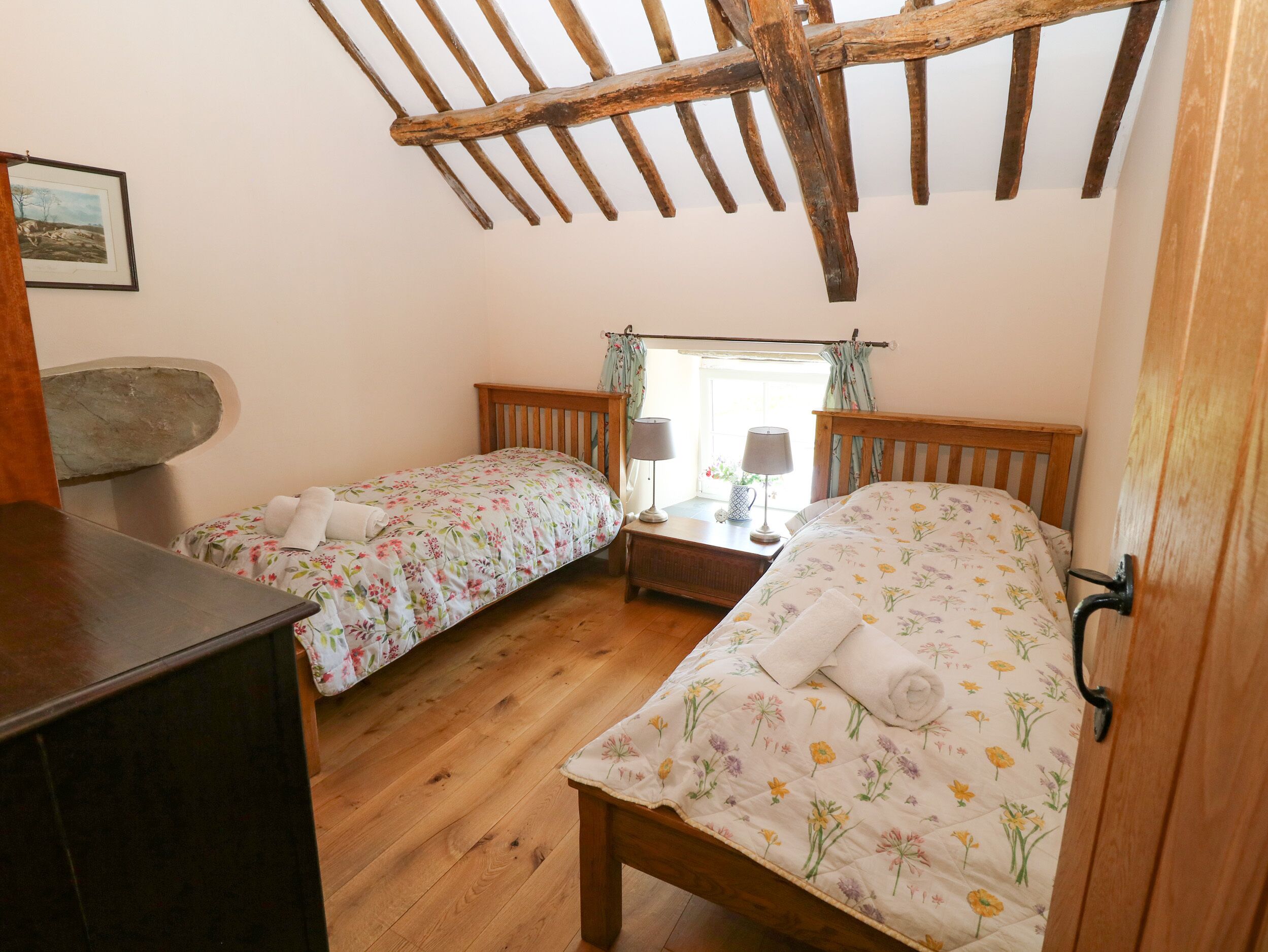 A bedroom with two single beds, wooden headboards, a stone bench, and a window with curtains.