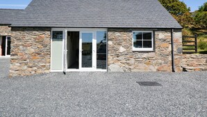 A stone building with a grey tiled roof, a gravel driveway, and a wooden fence in the background. - Garth Morthin The Farmhouse (Porthmadog)