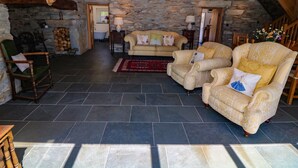 A rustic interior with stone walls, wooden beams, a stone fireplace, a sofa set, and a wooden chair. - Garth Morthin The Farmhouse (Porthmadog)