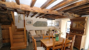 A rustic interior with exposed wooden beams, a dining area with wooden furniture, a sofa, and a stone wall. - Garth Morthin The Farmhouse (Porthmadog)