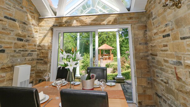 A dining area with a stone wall, a glass door leading outside, and a table set for two with a bottle of champagne.