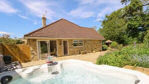 A hot tub in a backyard with a stone house and a wooden fence.