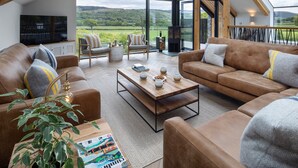 Un'ampia zona living con una grande finestra che si affaccia su un paesaggio verde. È presente un camino, posti a sedere confortevoli e un tavolino da caffè.