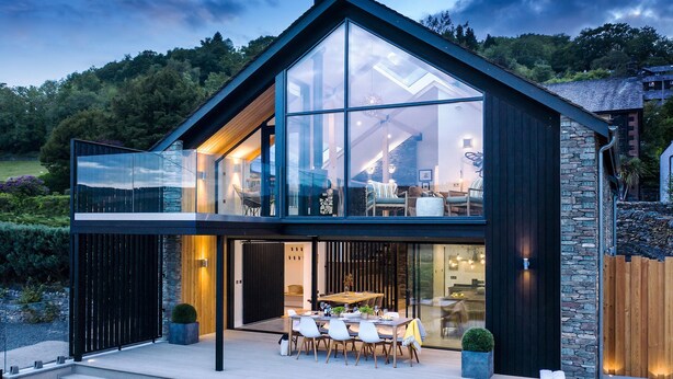 Una moderna casa a due piani con ampie vetrate, rivestimento in pietra e un patio con mobili da esterno.