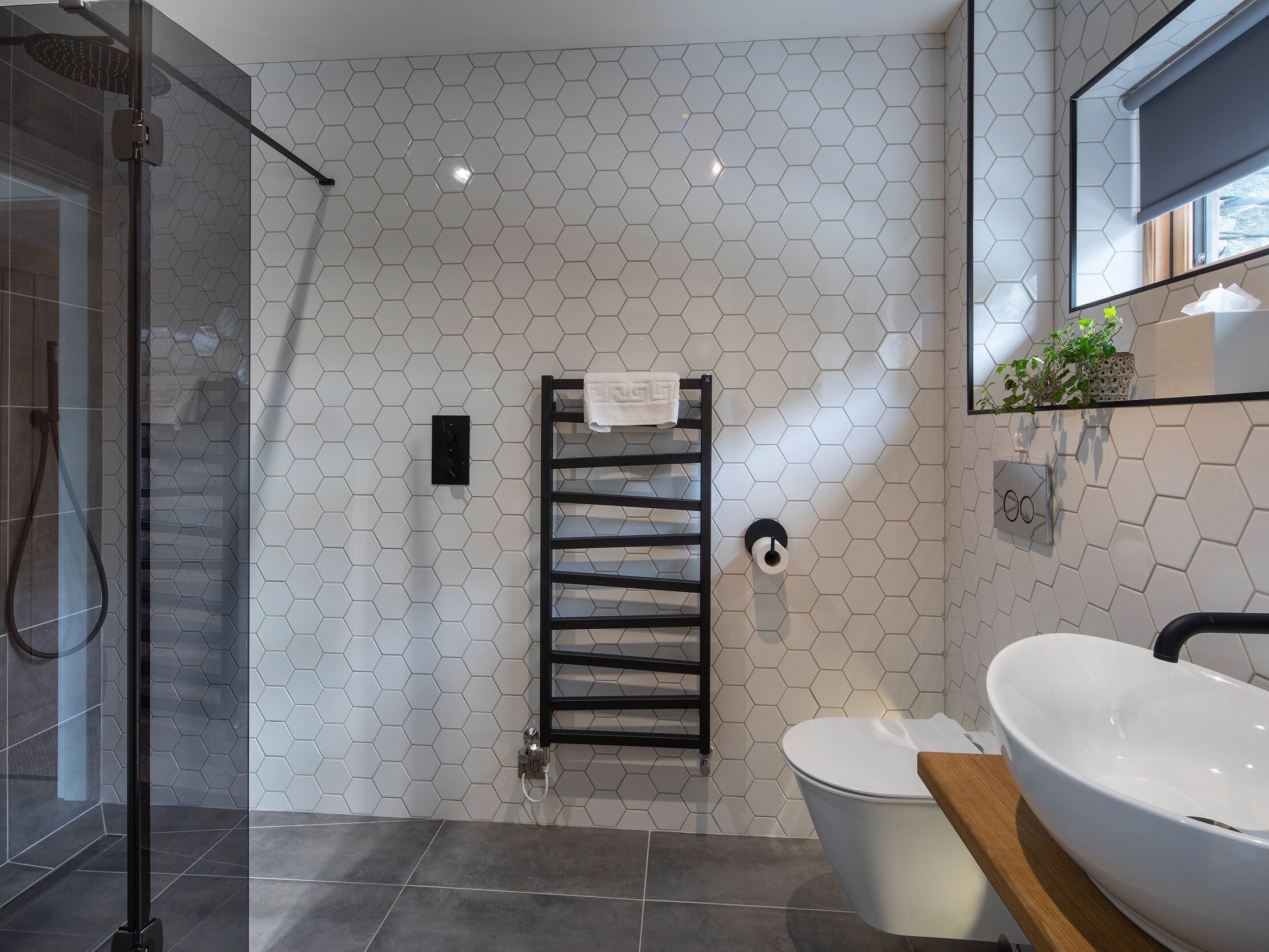 Une salle de bain moderne avec un carrelage à motifs hexagonaux, une douche en verre, un porte-serviettes noir, des toilettes et un grand lavabo blanc.