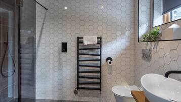 Une salle de bain moderne avec un carrelage à motifs hexagonaux, une douche en verre, un porte-serviettes noir, des toilettes et un grand lavabo blanc.