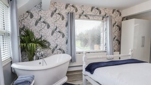Quarto com cama branca, guarda-roupa branco, banheira branca e janela com cortinas.