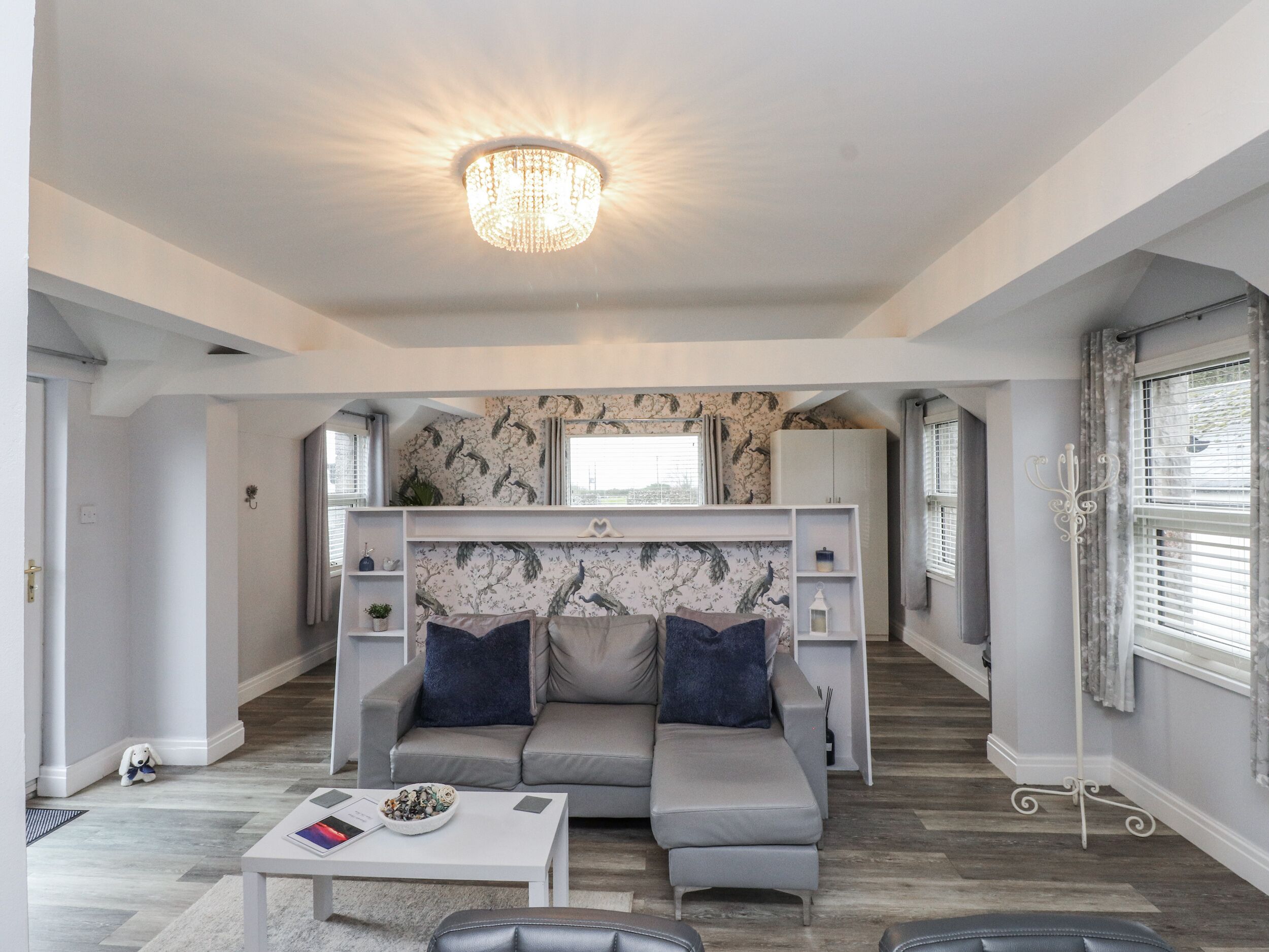 A modern living room with a grey sofa, a white coffee table, and a chandelier.