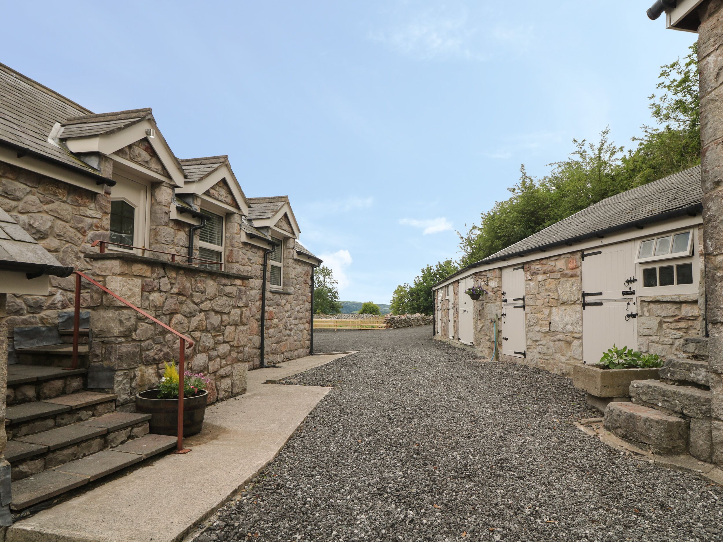 A stone building with a gravel driveway, a staircase, and a view of the landscape in the distance.