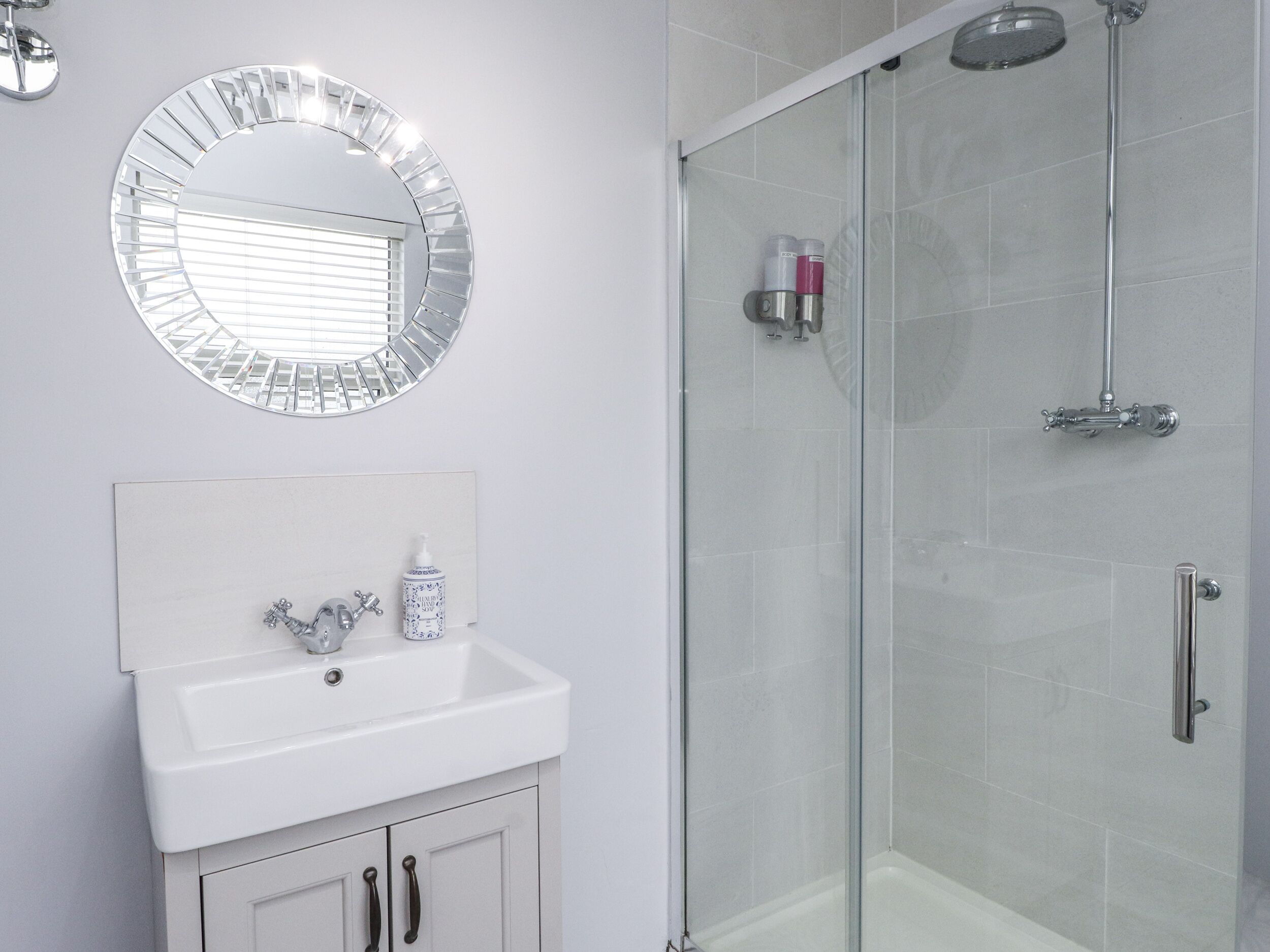 A bathroom with a glass shower enclosure, a white sink with a mirror above it, and toiletries on the sink.
