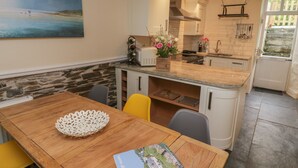 A kitchen with a wooden table, yellow chairs, a white island, and a painting on the wall. - Fairfield Cottage (Boscastle)