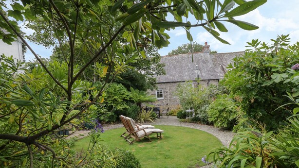 A garden with a lawn, a stone building, and a wooden chair. - Fairfield Cottage (Boscastle)