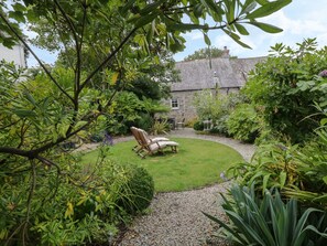 Un jardin avec une pelouse, un bâtiment en pierre et une chaise en bois.