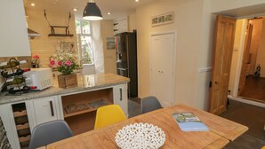 A compact kitchen with a dining area, featuring a wooden table, yellow chairs, and a white decorative bowl. - Fairfield Cottage (Boscastle)