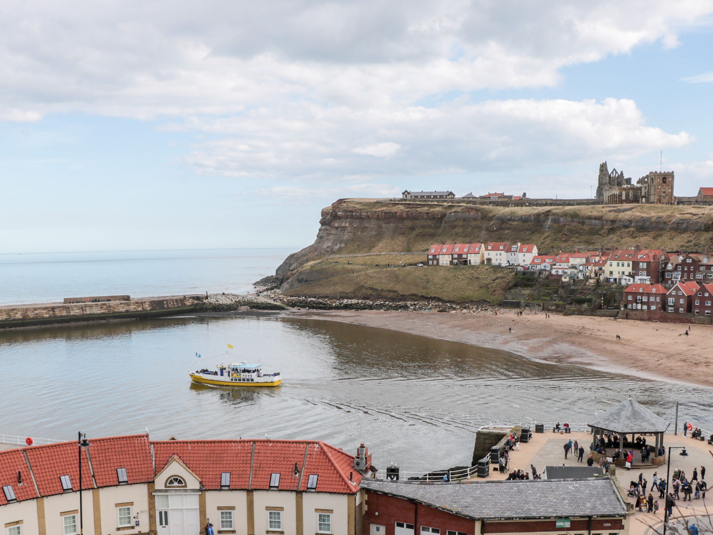 A coastal town with a historic castle on a cliff, a sandy beach, and a small boat on the water.