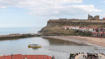 A coastal town with a historic castle on a cliff, a sandy beach, and a small boat on the water.