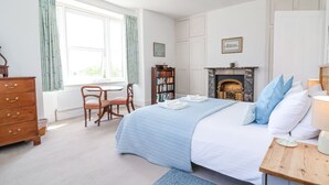 A bedroom with a bed, a wooden dresser, a chair, a bookshelf, a fireplace, and a window with curtains. - The Old Vicarage (Tiverton)