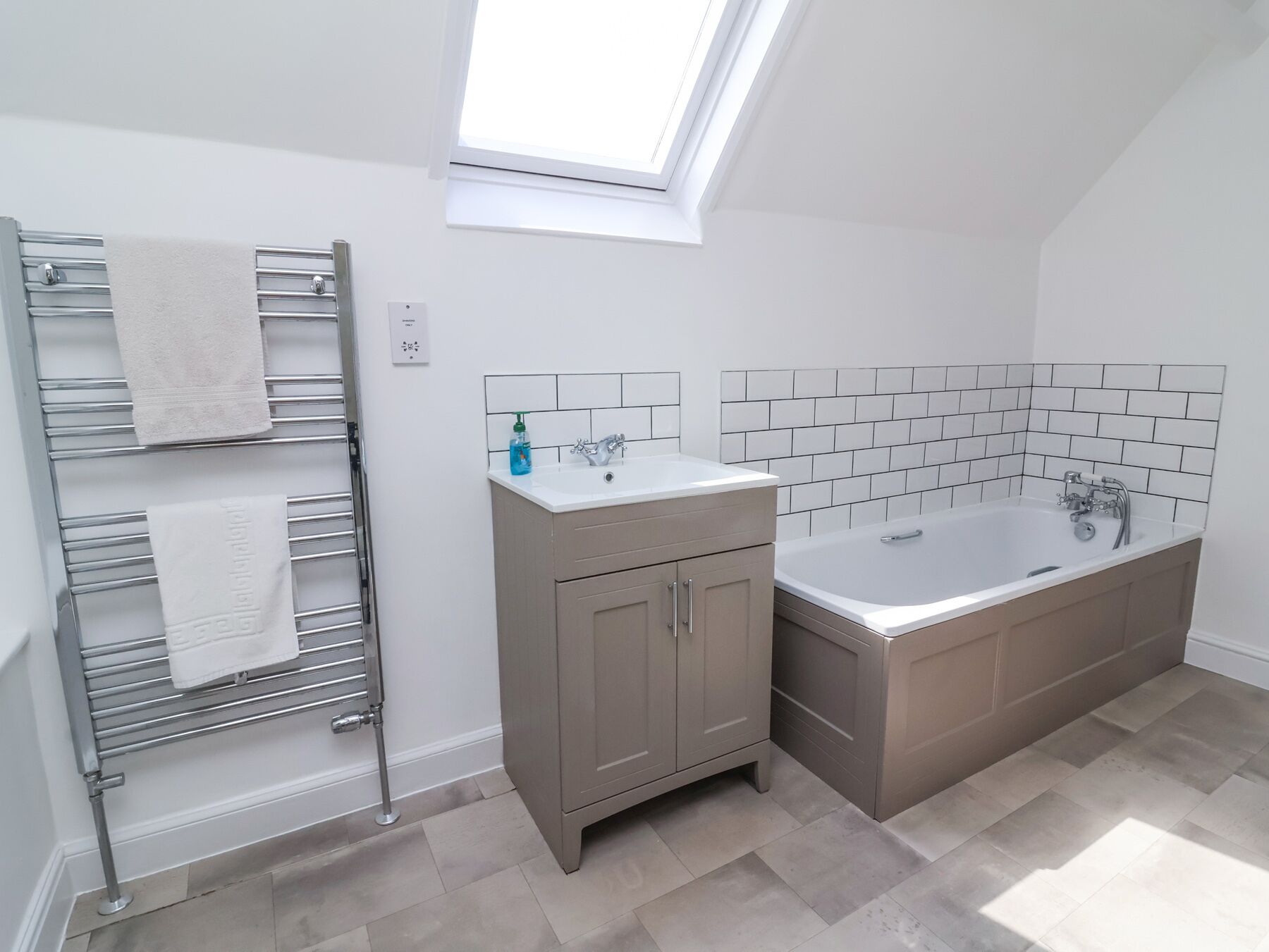 A modern bathroom with a skylight, a towel rack, a sink, and a bathtub.