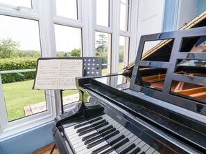 A grand piano with a music stand and sheet music in front of a large window overlooking a garden. - The Old Vicarage (Tiverton)