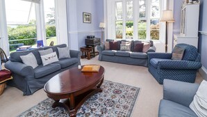 A spacious living room with a large window, a chandelier, and a fireplace. - The Old Vicarage (Tiverton)