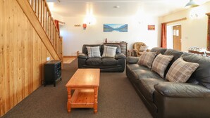 A living room with a wooden staircase, a black leather sofa, a wooden coffee table, and a painting on the wall. - The Dairy (Bude)