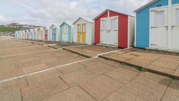 A row of colorful beach huts with white doors and windows, numbered sequentially, on a paved beach area. - The Dairy (Bude)