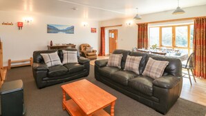 A living room with two black leather sofas, a wooden coffee table, and a dining area with a table set for four. - The Dairy (Bude)